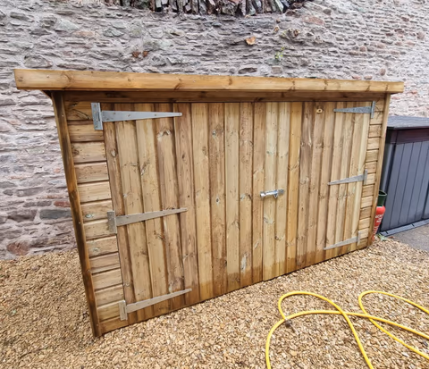 Low bespoke timber storage shed with two wide doors beside a stone wall