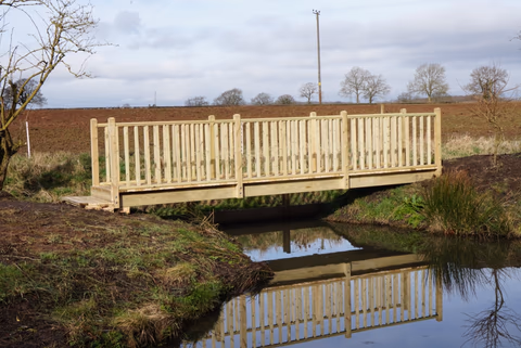 Bespoke timber footbridge with balustrades crossing a stream